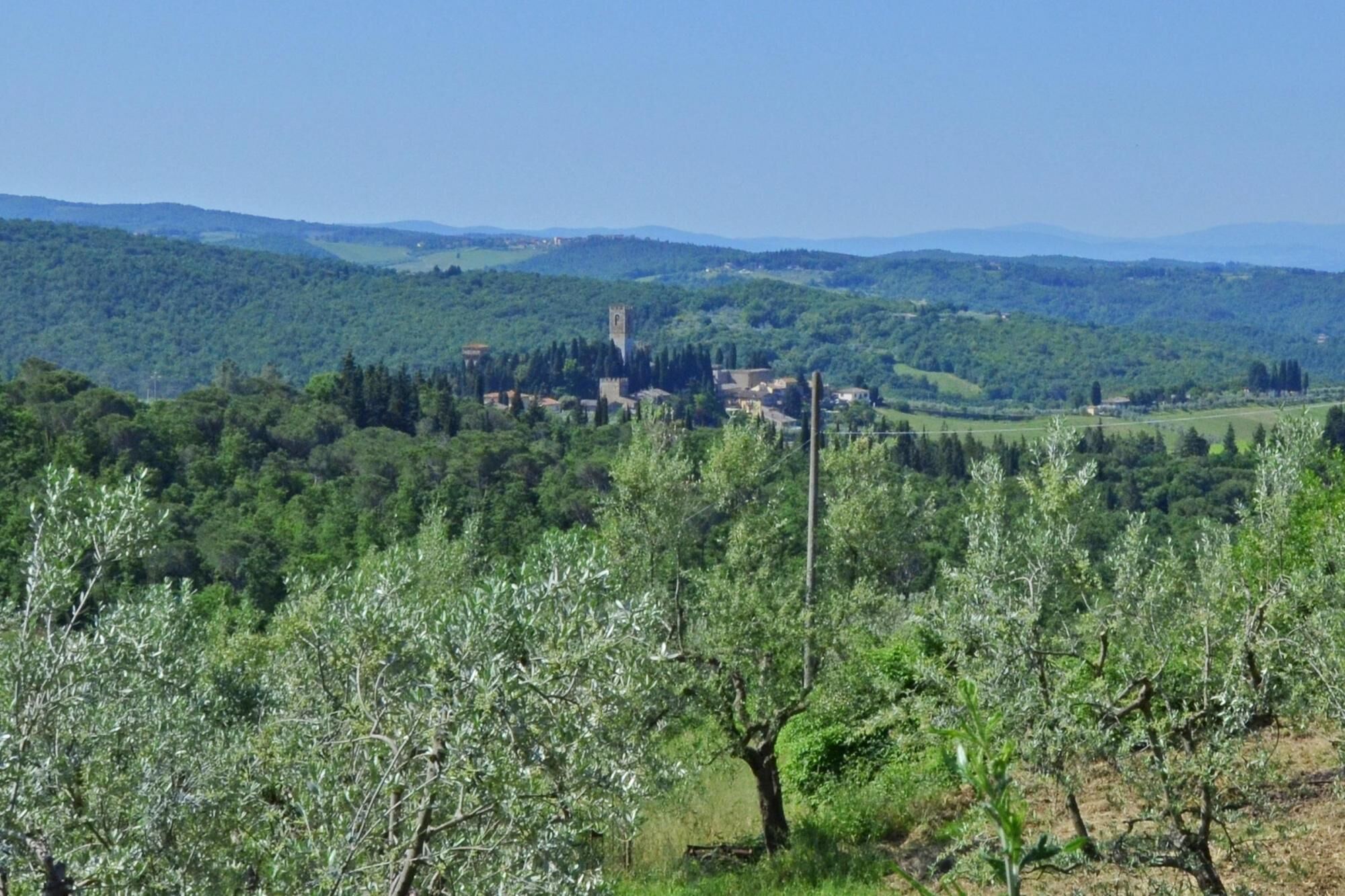 A rural landscape with a village, olive groves, and rolling hills in the background.