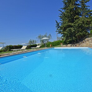 Ein klares, blaues Schwimmbecken mit Liegestühlen und Sonnenschirm, umgeben von Grünpflanzen und einer Steintreppe.