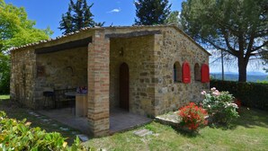 A stone building with a covered patio, a small table, and chairs. - La Badia 2 in Tavarnelle Val di Pesa (Barberino Tavarnelle)