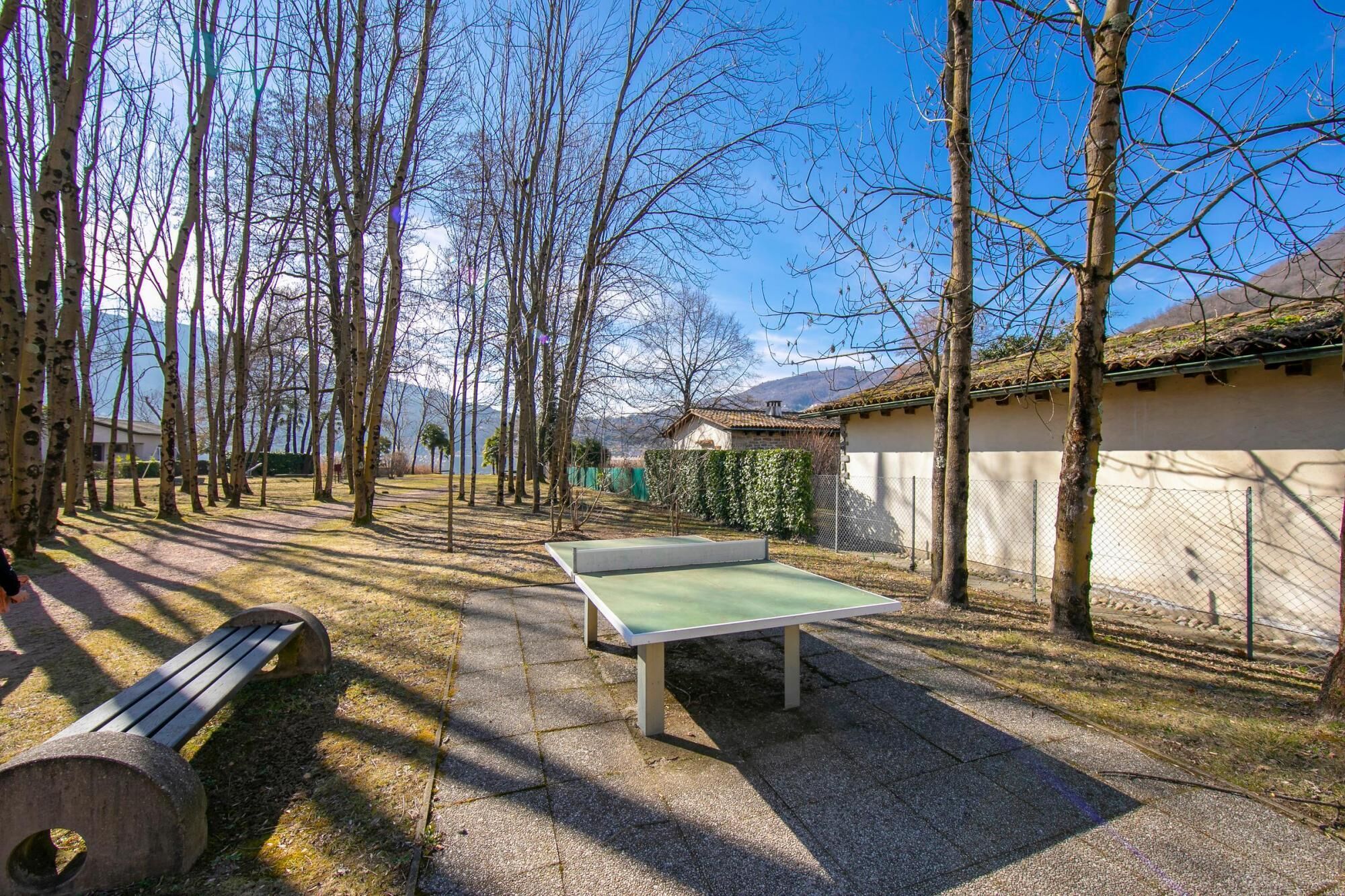 Egy szabadtéri terület, ahol van egy pingpongasztal, egy pad és egy kőből épített szerkezet.