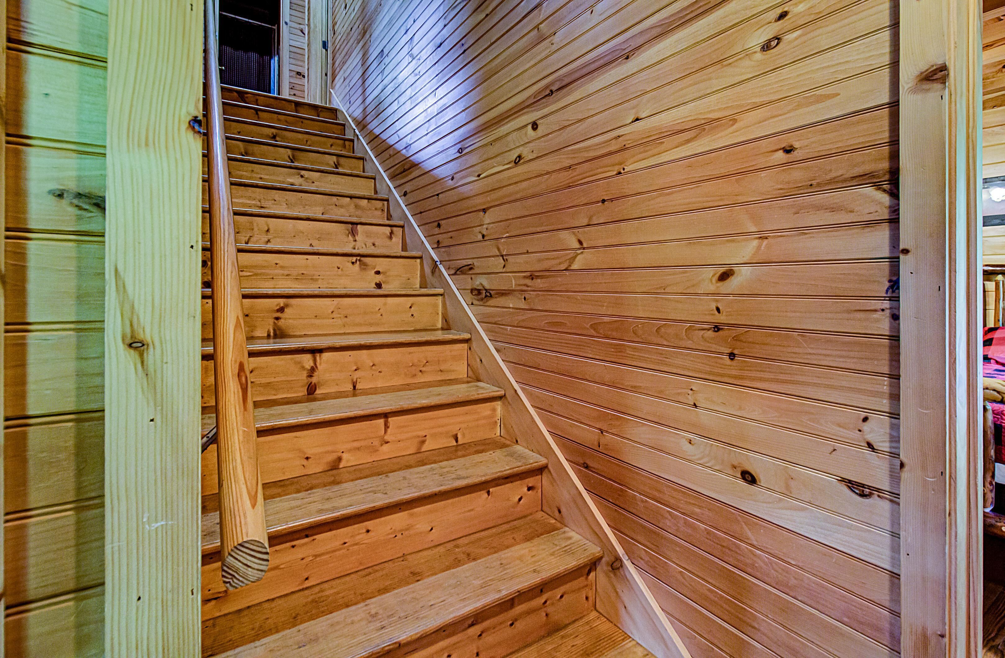 A wooden staircase with a metal handrail, leading to a room with wooden walls.