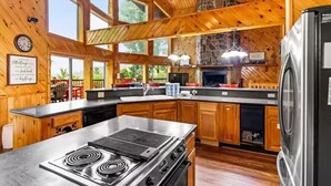 A spacious kitchen with wooden cabinets, a large island with a stove, and a stone fireplace. - Big Sky Lodge #438 (Sevierville)