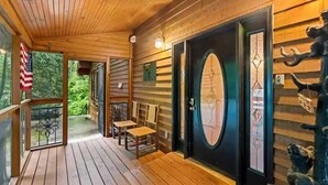 A wooden porch with a black door, two chairs, and an American flag. - Big Sky Lodge #438 (Sevierville)