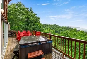 A wooden deck with a hot tub, red chairs, and a table.