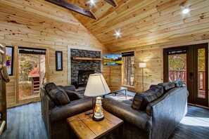 A cozy cabin interior with wooden walls, a stone fireplace, leather sofas, and a table with a lamp. - Wilderness Waterland #2161 (Sevierville)