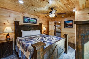A wooden cabin bedroom with a bed, two bedside lamps, a ceiling fan, and two framed pictures on the walls. - Wilderness Waterland #2161 (Sevierville)