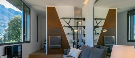 A modern living room with a sofa, a coffee table, and a TV. There is a large window with a view of mountains.
