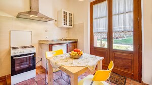A kitchen with a stove, oven, and cabinets. There is a table with a fruit bowl and chairs. - Pomegranate apt With Shared Pool (Castiglione del Lago)