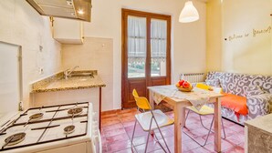 A compact kitchen with a gas stove, a sink, and a dining area with a table and chairs. - Pomegranate apt With Shared Pool (Castiglione del Lago)