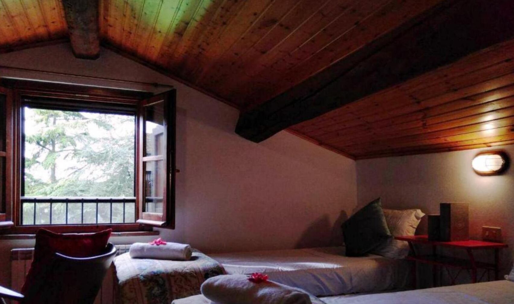 Une pièce chaleureuse avec un plafond en bois, un lit avec des oreillers, une petite table et une fenêtre donnant sur des arbres.