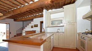 Una cocina con vigas de madera, una isla central, armarios blancos, salpicadero de azulejos y una estufa.