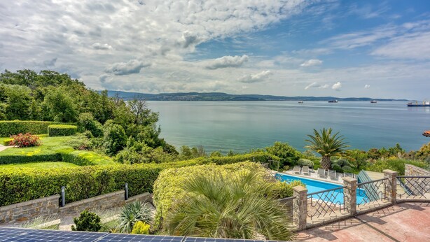 A landscaped garden with a pool, overlooking a calm body of water with boats. - Pool Apartment Debeli Rti 3 (Ankaran)