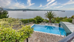 A swimming pool with a view of the sea and boats, surrounded by greenery and a stone patio. - Pool Apartment Debeli Rti 3 (Ankaran)
