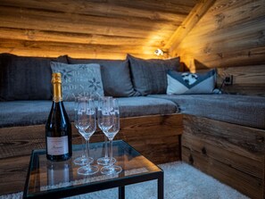 A wooden cabin interior with a glass table holding a bottle and four glasses.
