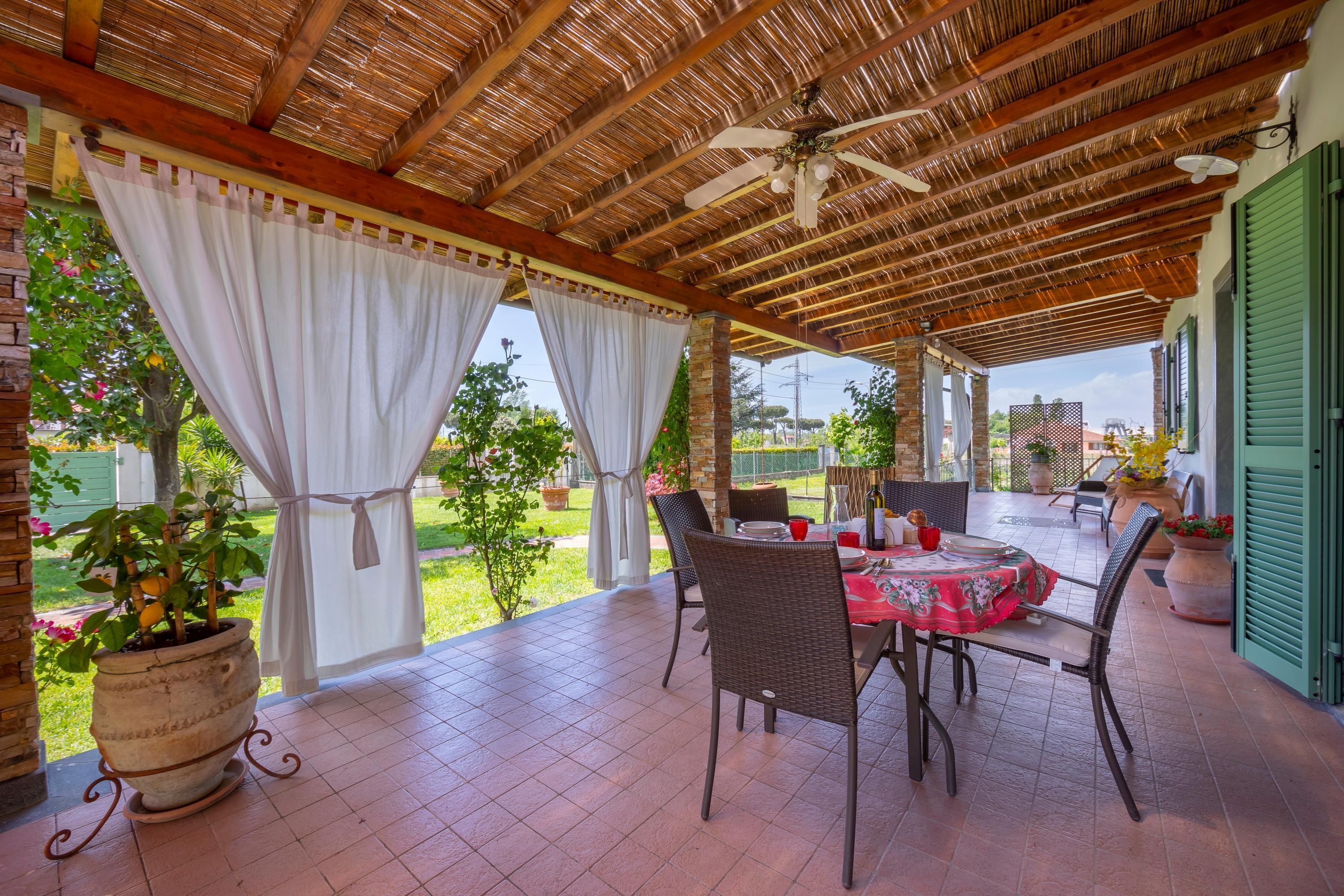 Eine überdachte Terrasse mit Tisch, Stühlen, einem Deckenventilator und Kübelpflanzen.