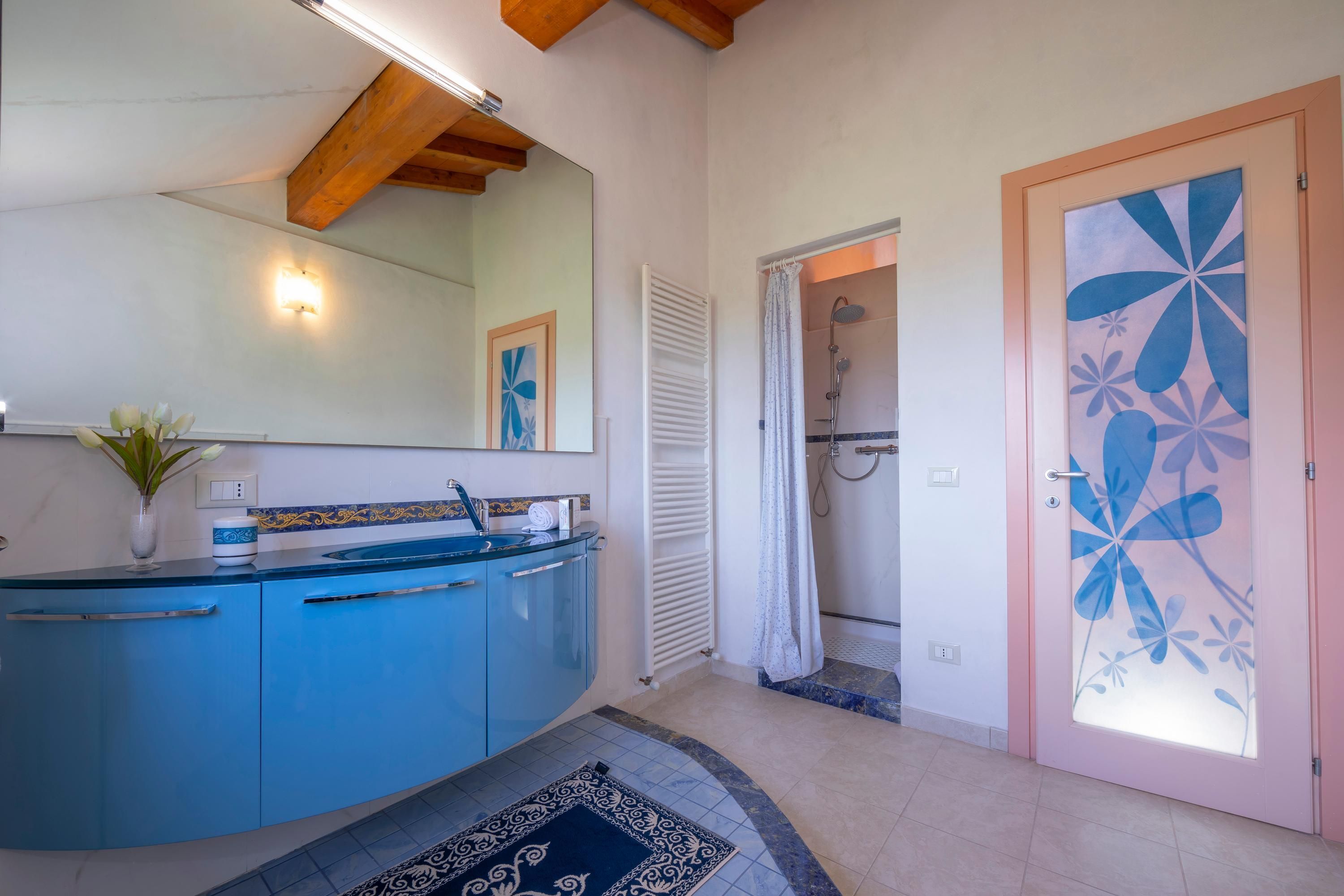 Une salle de bain avec un meuble-lavabo bleu, un radiateur blanc, un espace douche et une porte ornée de motifs floraux.