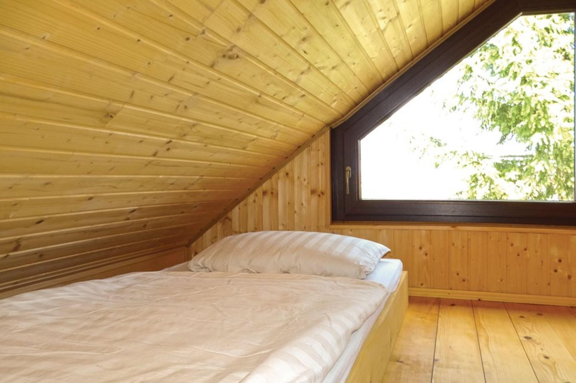 Ein Schlafzimmer mit schrägem Dach und einem Fenster mit Blick auf Grünflächen.