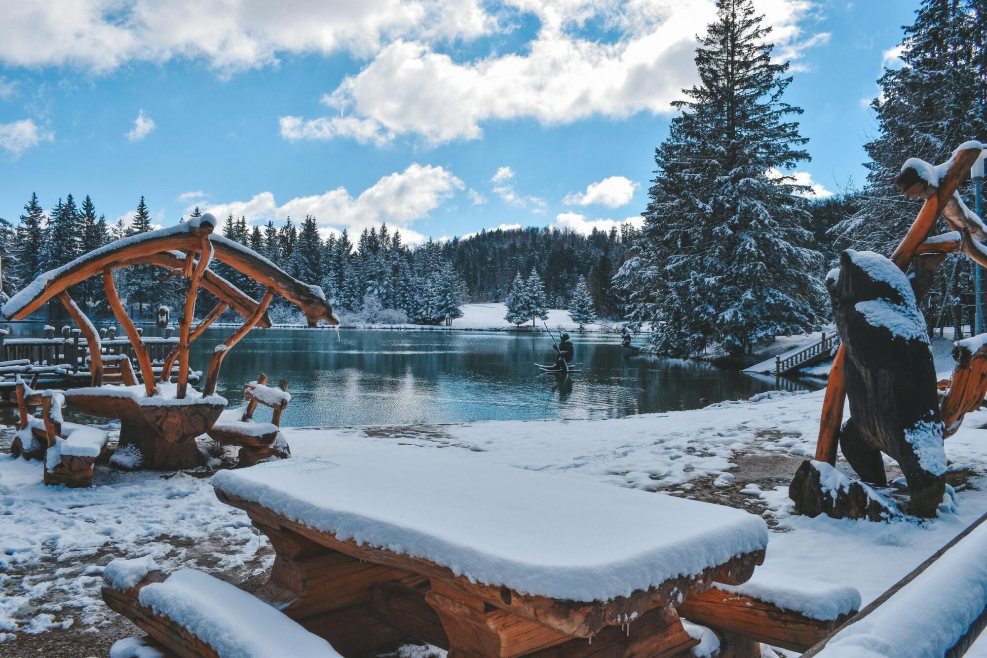 A wooden dock extending into a lake, surrounded by snow-covered trees and a clear sky.