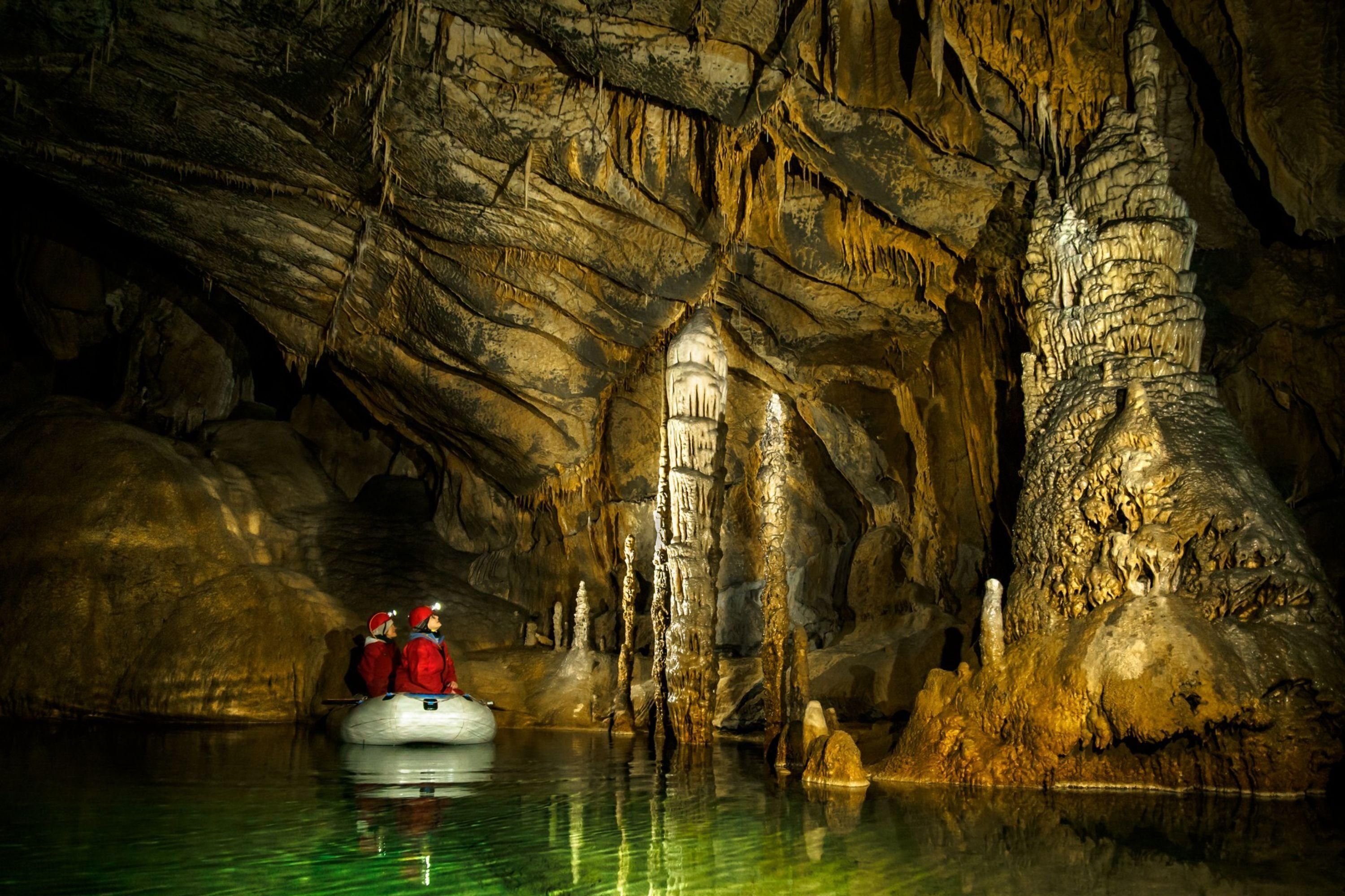 Una grotta con stalattiti e stalagmiti, una barca con persone e un corso d'acqua.