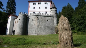 Un château avec un mur de pierre, une tour et une meule de foin au premier plan.
