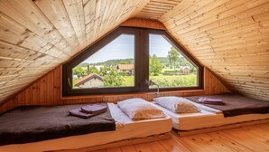 Une chambre mansardée chaleureuse, avec des murs en bois et une grande fenêtre donnant sur la campagne.