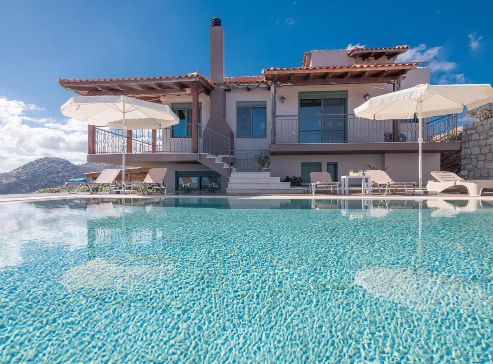 A modern two-story house with a swimming pool, outdoor seating, and a mountain backdrop.