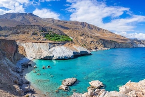 A coastal landscape with rocky cliffs, clear turquoise waters, and a mountainous backdrop. - Villa Eolos Crete in Heraklion (Malevizi)