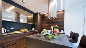 A modern kitchen with dark wood cabinetry, a central island with fresh produce, and a sleek stainless steel range hood. - Rebecca Garden in Lugano (Lugano)