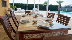 Mesa de comedor al aire libre con sillas, una piscina y un área cubierta al fondo.