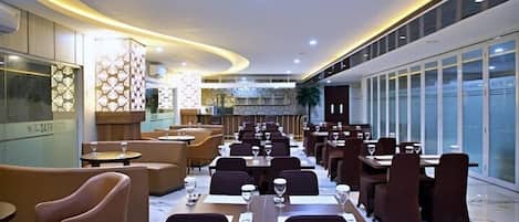 Un restaurante espacioso con techos altos, iluminación moderna y diversas opciones de asientos, incluyendo mesas y cabinas.