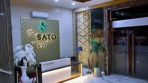 A reception area with a reception desk, a decorative wall with the hotel's name, and a potted plant. - THE SATO HOTEL (Kudus)