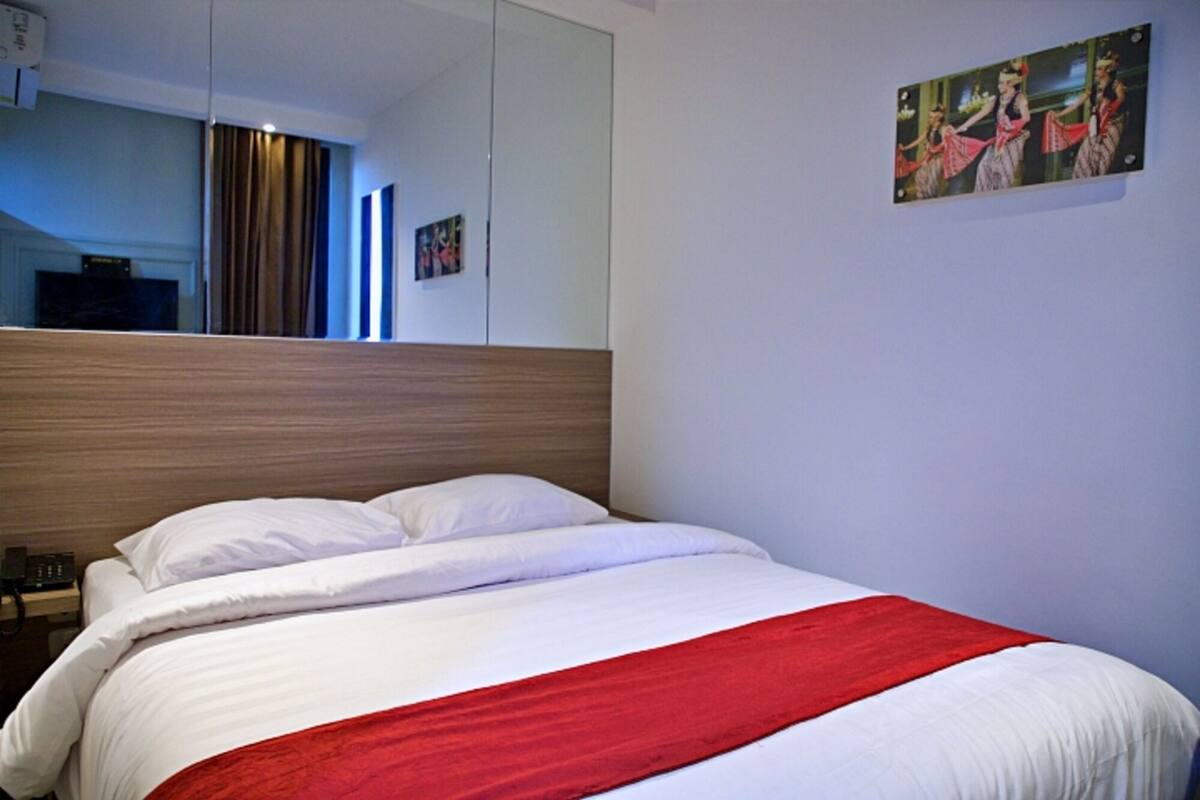 Una habitación de hotel con una cama grande, cabecera de madera, una manta roja y un cuadro en la pared.