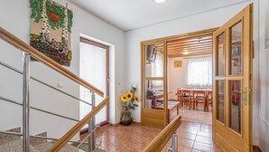 Un escalier doté d’une rampe en bois et de balustrades en métal, menant à un espace repas avec des tables et des chaises en bois.