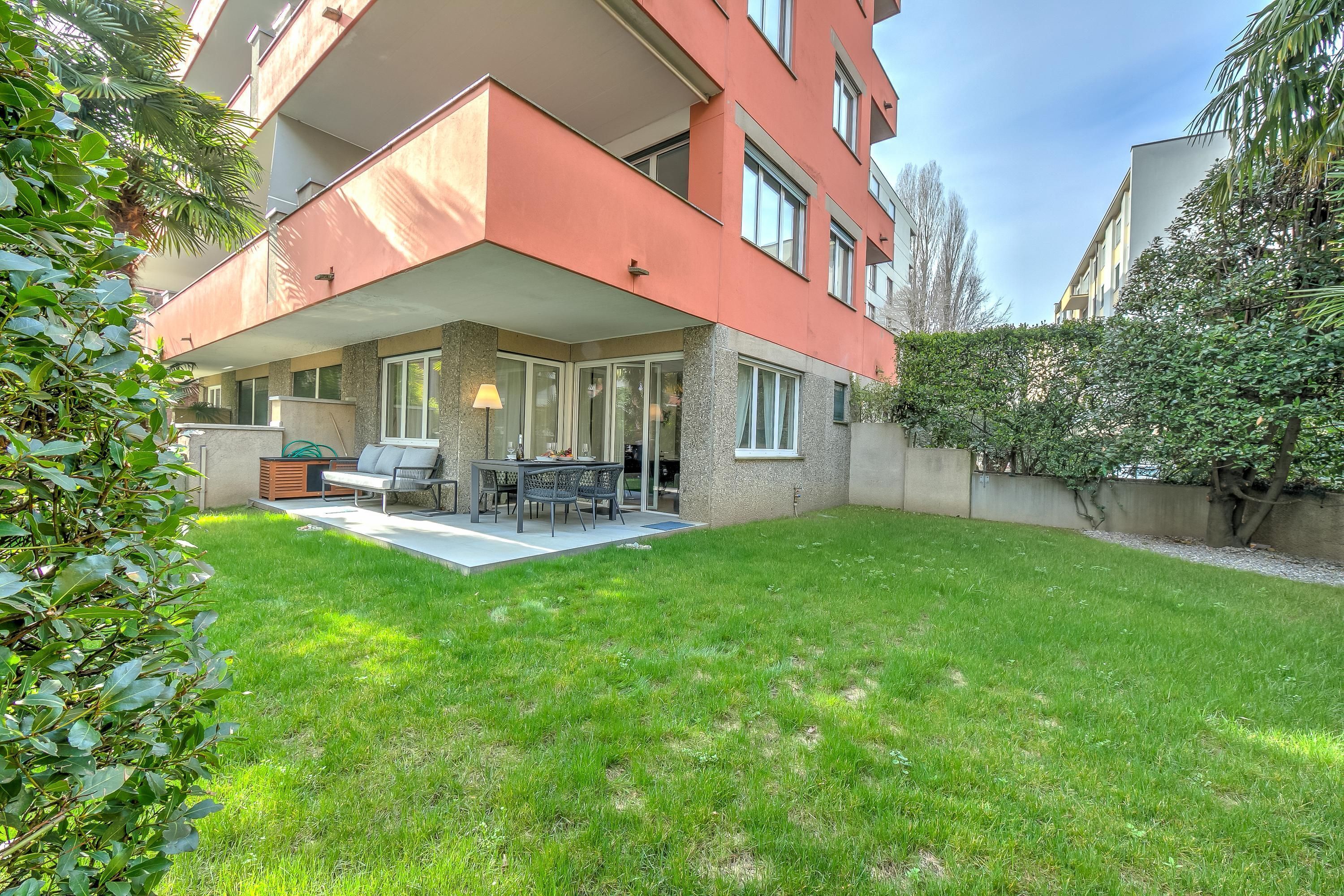 A modern apartment with a covered patio, outdoor seating, and a well-maintained lawn.