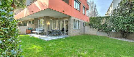 A modern apartment with a covered patio, outdoor seating, and a well-maintained lawn.
