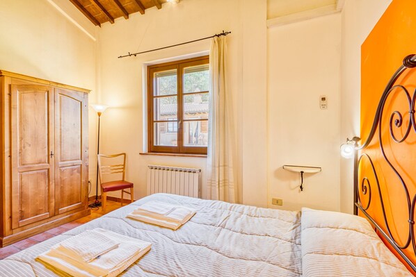 A bedroom with a bed, wooden wardrobe, chair, window, radiator, and wall-mounted light fixture.