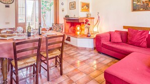 A dining area with a wooden table and chairs, a red sofa, and a fireplace. - Hawthorn apt With Shared Pool Family fun (Castiglione del Lago)