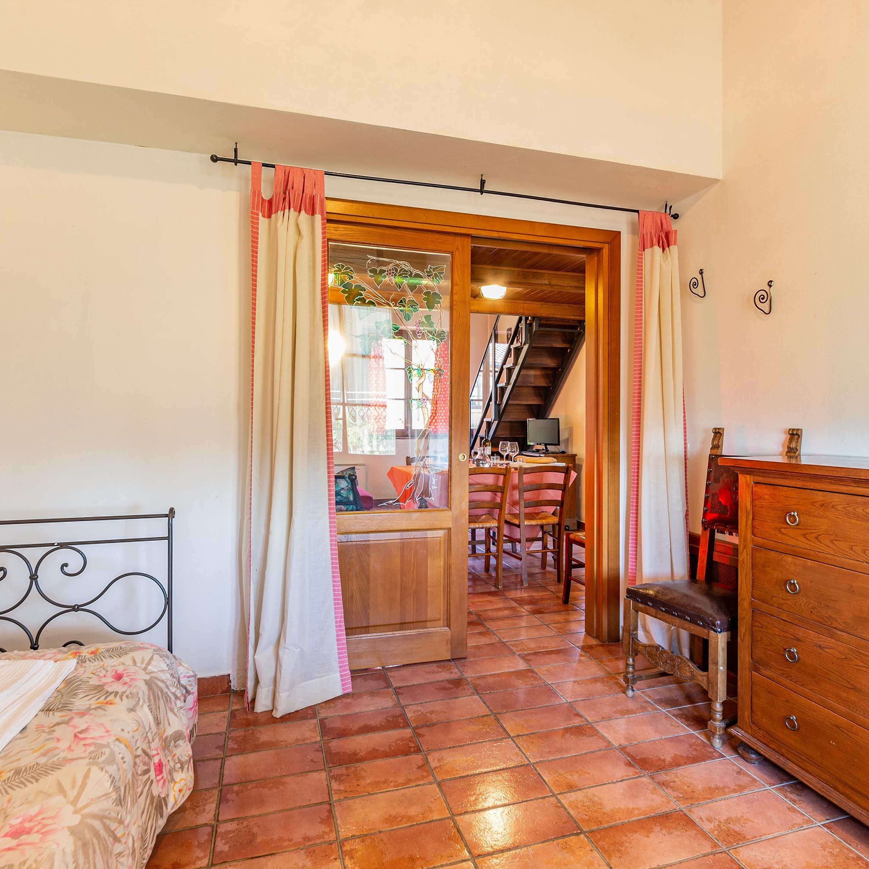 Una camera da letto con un letto, una cassettiera in legno, un tavolo da pranzo con sedie e una scala che conduce a un'altra stanza.