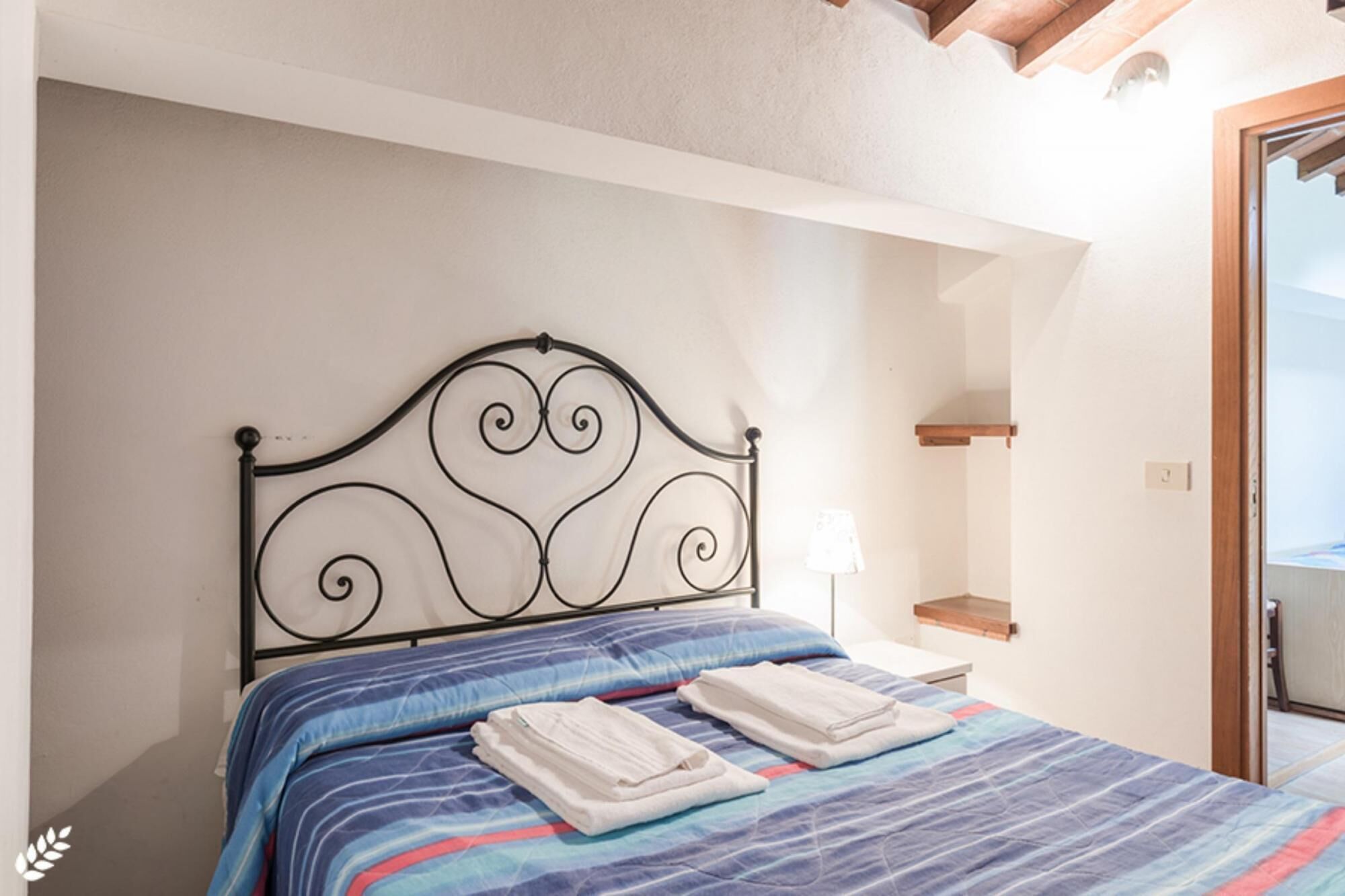 A neatly made bed with a blue and red striped bedspread, a black metal headboard, and two folded white towels.