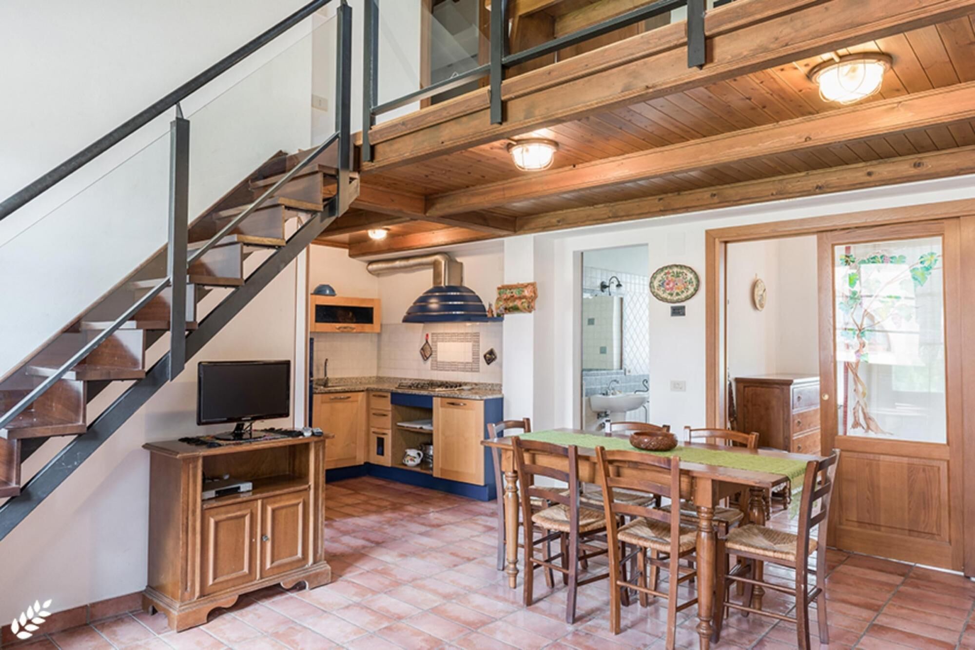 A kitchen with wooden cabinets, a dining table with chairs, and a staircase with metal railings.