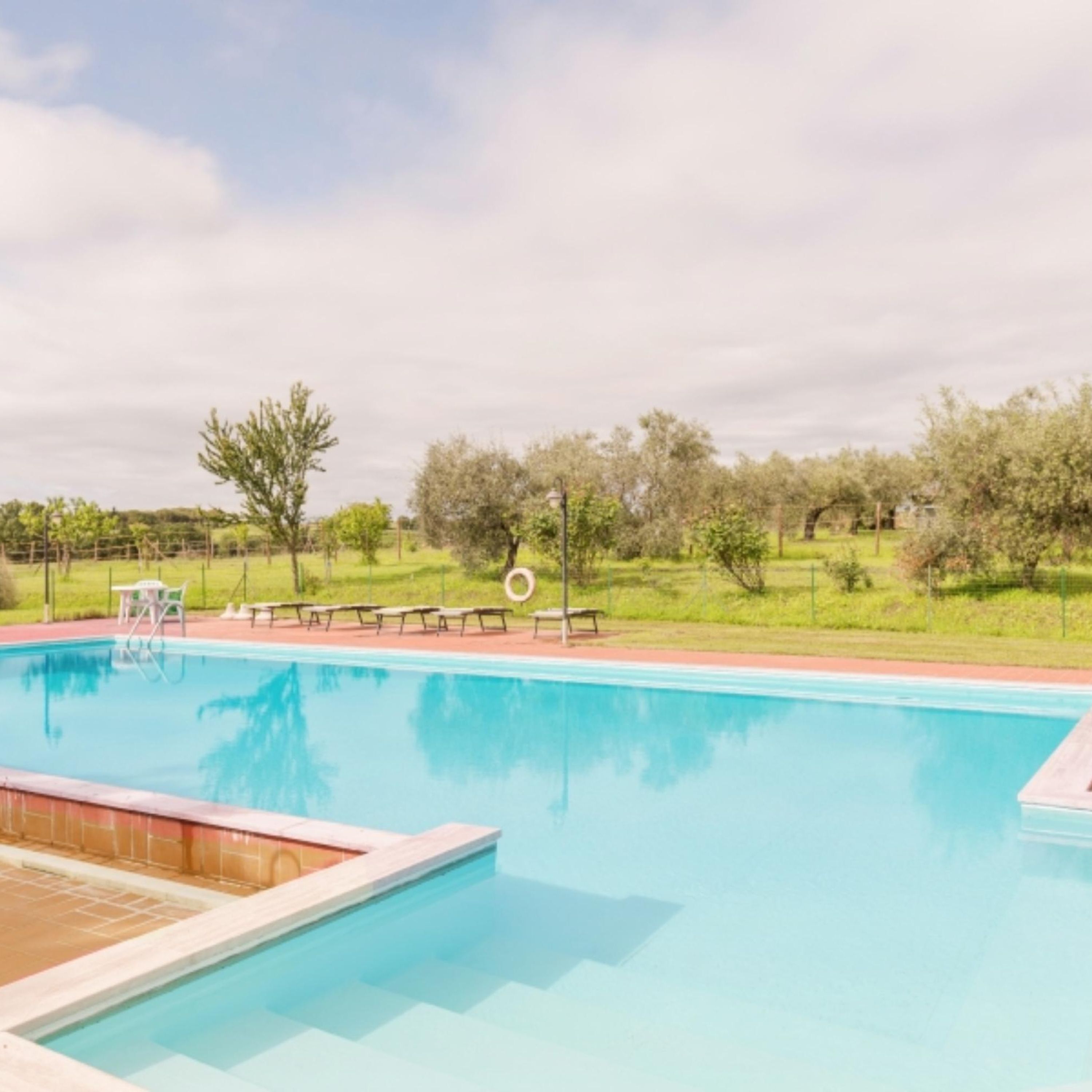 Una piscina rectangular amb un voreig de fusta, envoltada per una paret baixa de maó.