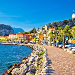 A coastal town with colorful buildings, a stone promenade, and parked cars along the waterfront.