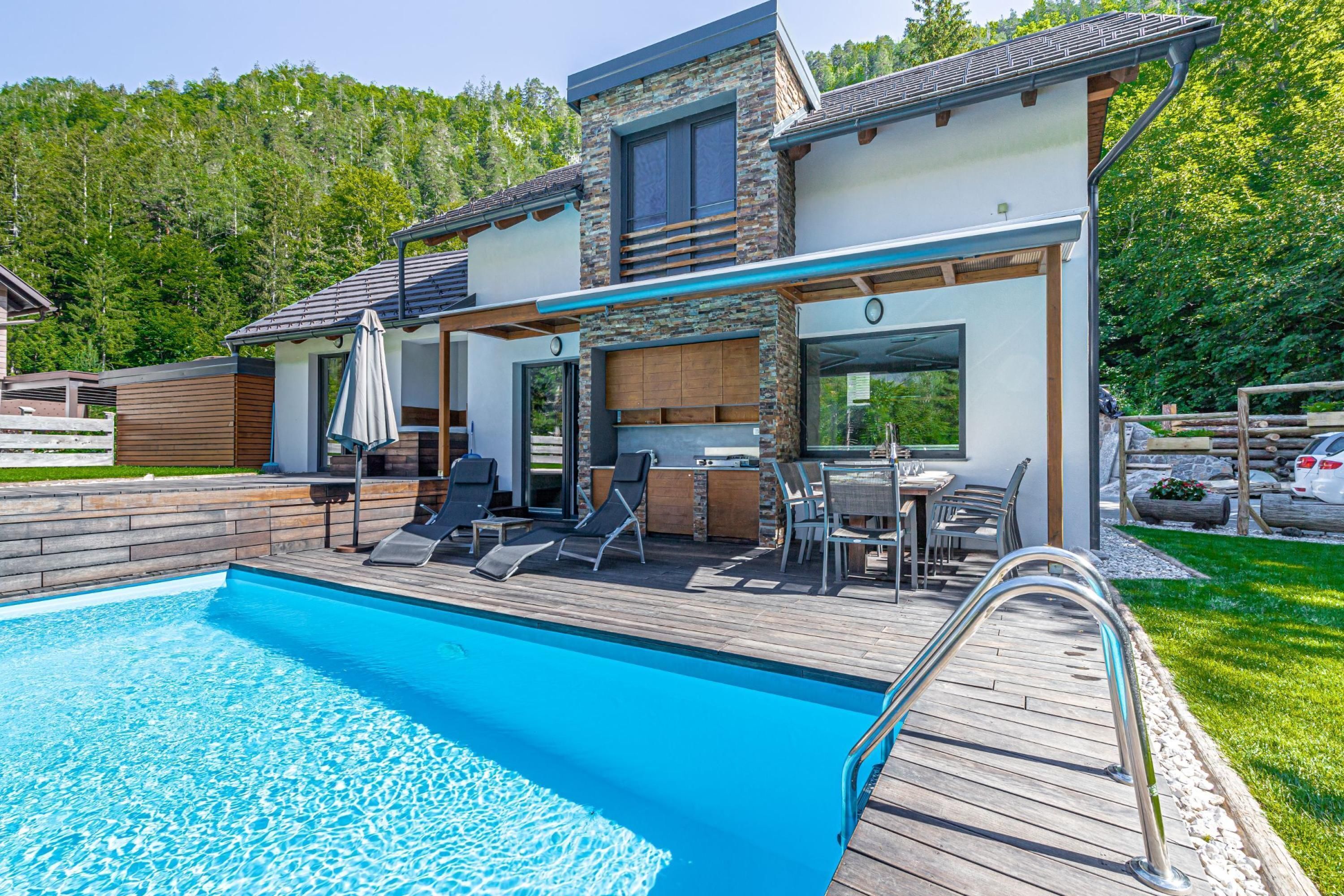 Una casa moderna con piscina, mobiliario exterior y vistas al bosque.