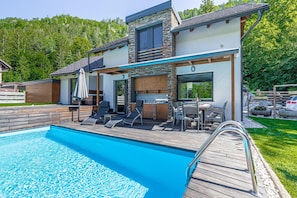 A modern house with a swimming pool, outdoor seating, and a view of the forest.