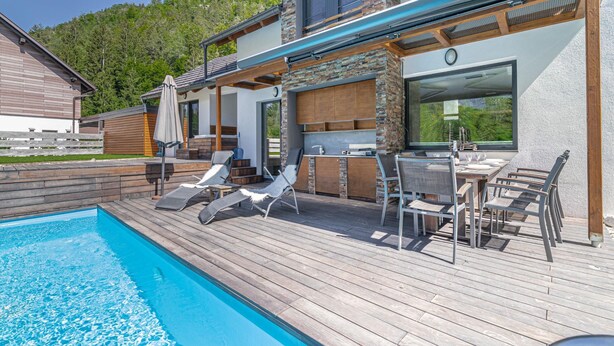 A poolside area with a wooden deck, lounge chairs, a barbecue grill, and a stone wall. - Pool Villa Katja Kranjska Gora (Kranjska Gora)