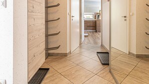 A hallway with a wooden wall, a metal rack, and a tiled floor leading to a kitchen area. - Pool Villa Katja Kranjska Gora (Kranjska Gora)