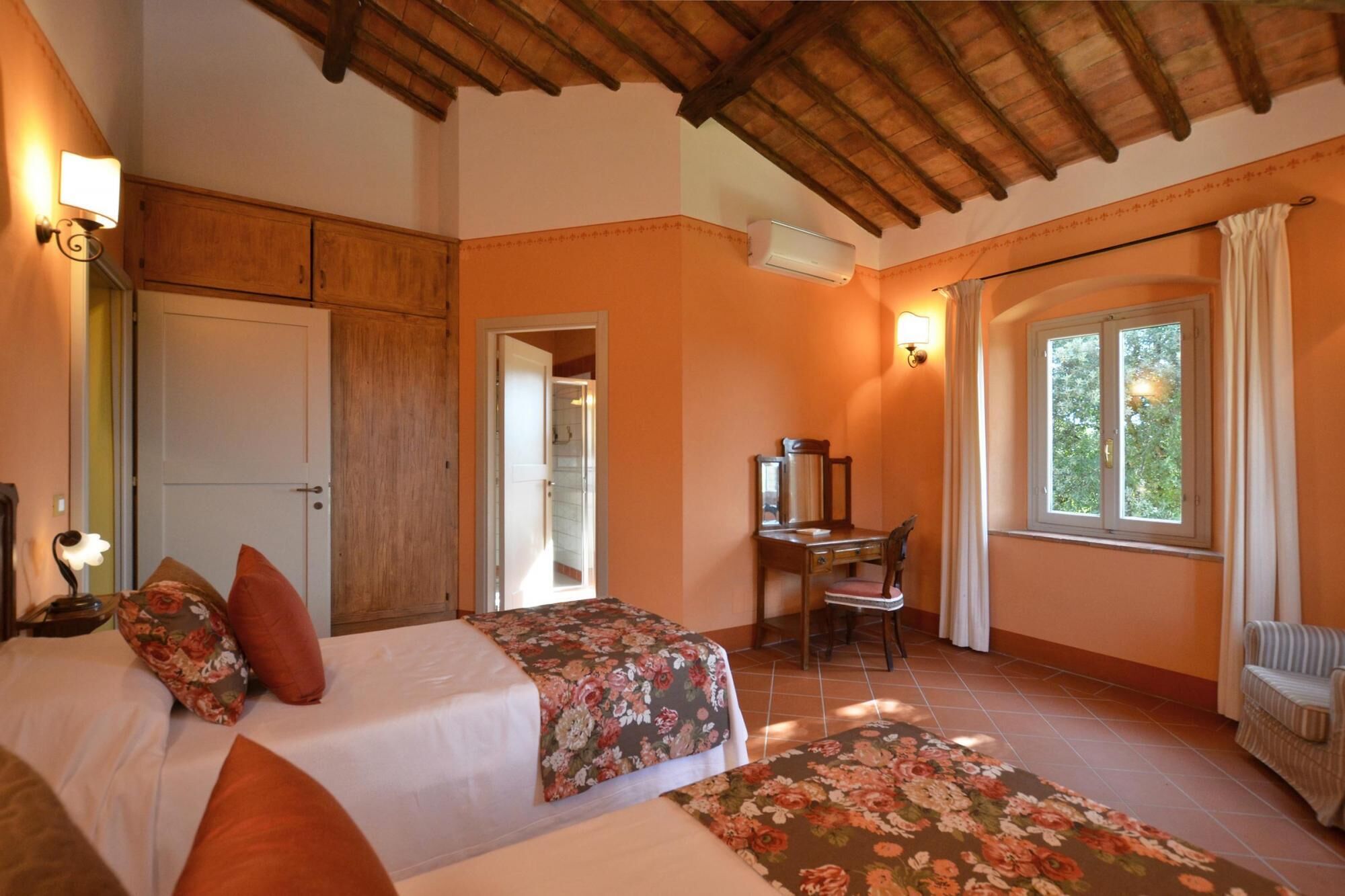 Un dormitorio con dos camas, un escritorio y una silla. Se ve una ventana con cortinas y un equipo de aire acondicionado en la pared.