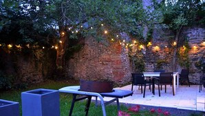 Une terrasse extérieure avec des murs en pierre, des guirlandes lumineuses et une table entourée de chaises.