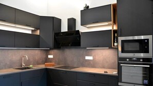 Une cuisine moderne avec des meubles de couleur sombre, un évier en acier inoxydable et des appareils électroménagers intégrés, notamment un four à micro-ondes et un four traditionnel.