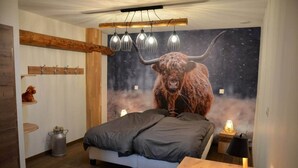 Une chambre avec un grand lit, des poutres en bois, un mur rustique, une fresque représentant un taureau et un luminaire suspendu.